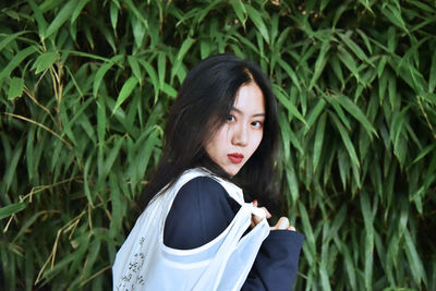 Portrait of young woman standing against plants