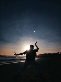 Rear view of silhouette man sitting at beach during sunset