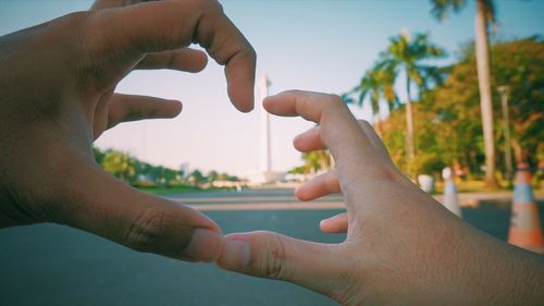 Close-up of man holding hands against sky