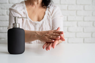 Midsection of woman holding bottle against white wall