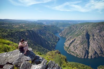 Rear view of woman sitting on rock against sky