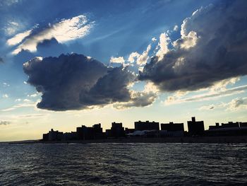 Silhouette city by sea against sky during sunset