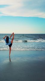 Rear view of woman exercising on shore at beach