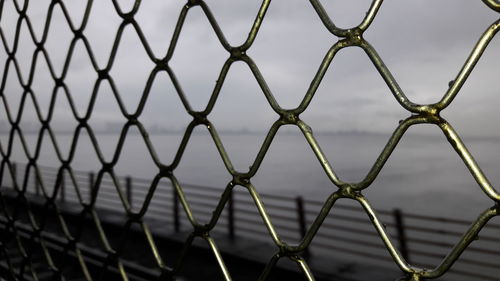 Sea seen through chainlink fence against sky