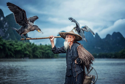 Birds perching on stick held by man in lake
