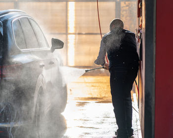 Rear view of mechanic washing car at garage