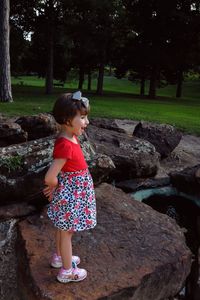 Full length of cute girl standing on rock against trees in park