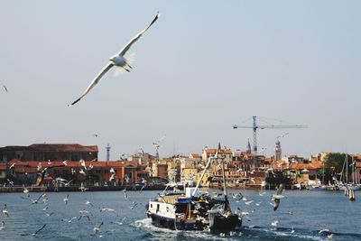 Boat in river with buildings against clear sky