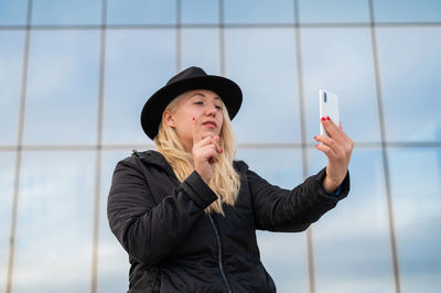 Young woman using mobile phone while standing on mirror