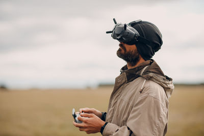 Man holding camera while standing against sky