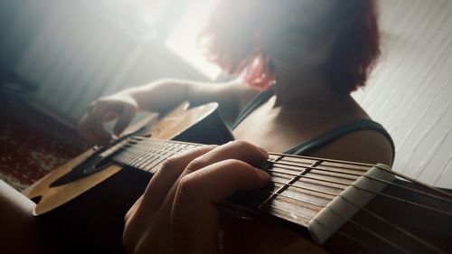 Midsection of woman playing guitar at home