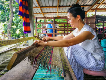 Side view of smiling woman weaving carpet at workshop