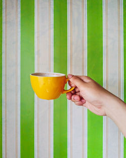 Cropped image of hand holding coffee cup on window