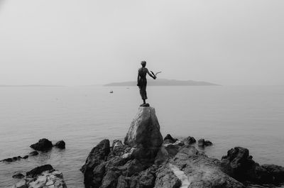 Man standing on rock by sea against sky