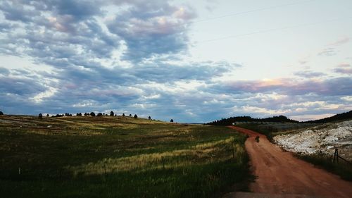 Road passing through field against cloudy sky