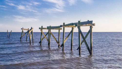 Wooden posts in sea against sky