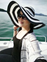 Portrait of smiling young woman wearing sunglasses sitting on boat against lake