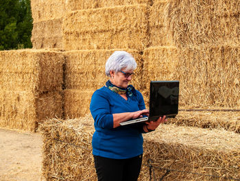 Woman using laptop while standing by hay bales