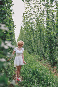 Woman in white dress standing on field amidst trees