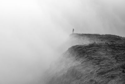 Silhouette person standing on mountain during foggy weather