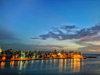 Illuminated buildings by sea against sky at night