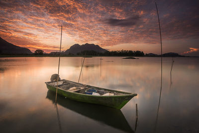 Boat moored in lake against sky during sunset