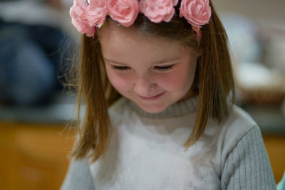 Girl with a red flower headband looks down smiling