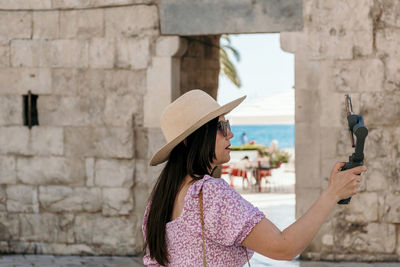 Side view of woman holding mobile phone against wall