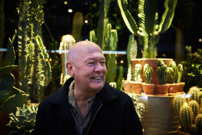 Smiling senior man sitting against succulent plant store at night