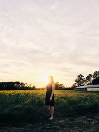 Rear view of man standing on field against sky during sunset