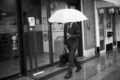 Full length of man with umbrella walking in city during rainy season