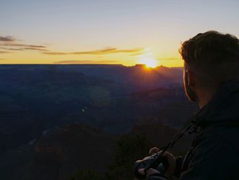 Rear view of man looking at mountains during sunset