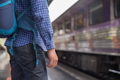 Midsection of man wearing backpack standing railroad station platform
