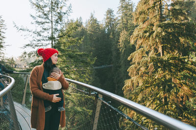 Mother carrying daughter while standing on footbridge against trees during winter