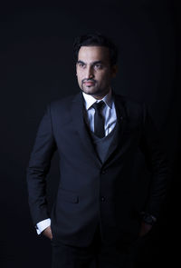 Portrait of young man standing against black background