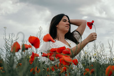 Portrait of beautiful young woman wearing white dress, standing in poppy field