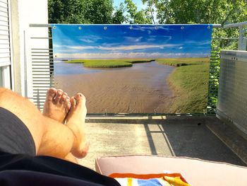 Low section of man relaxing by window against sky