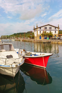 Boat moored in lake by buildings against sky