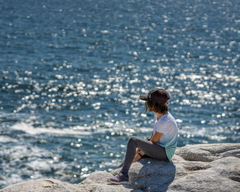 Rear view of woman sitting on rock at beach