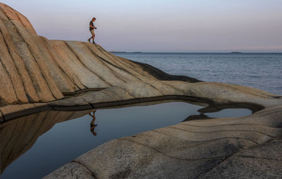 Man standing on rock by sea against sky