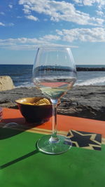 Close-up of wineglass on table at beach against sky