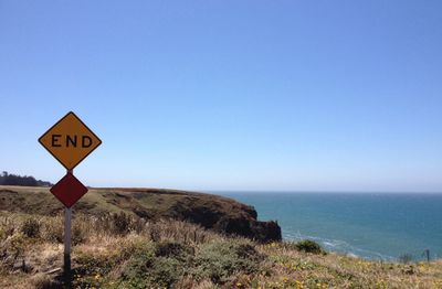 Road sign by sea against clear blue sky