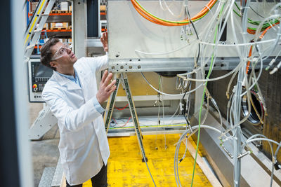 Man wearing lab coat and safety goggles examining at machine