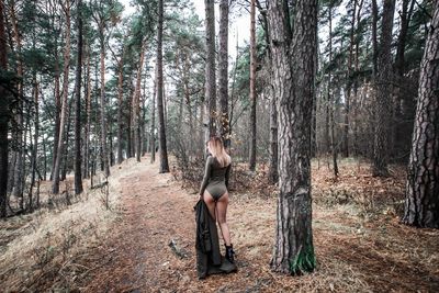 Woman sitting on tree trunk amidst plants in forest