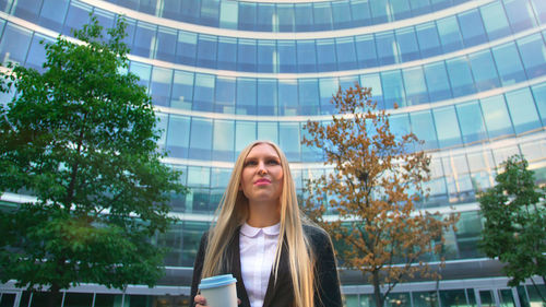 Portrait of woman standing against trees in city