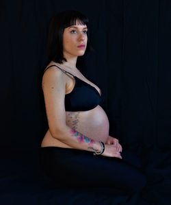 Side view of pregnant woman sitting against black background