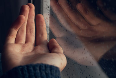 Cropped hand reflecting on wet window