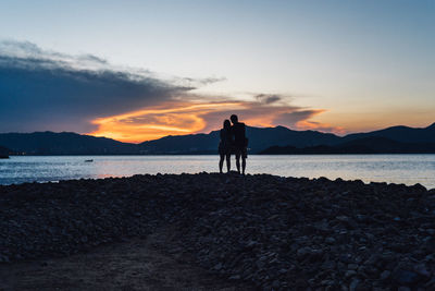 Silhouette men standing on beach against sky during sunset