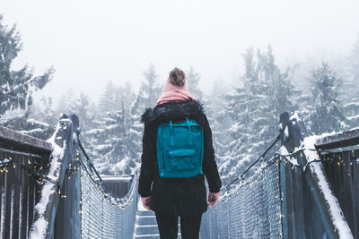 Rear view of woman standing on footbridge during winter