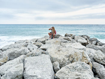 Woman sitting on rock by sea against sky